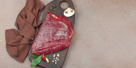 Fresh raw flank steak with assorted spices on wooden cutting board. Culinary concept for meat preparation, gourmet cooking, or food styling, banner formatの写真素材