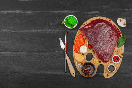 Gourmet food concept with raw flank steak, assorted spices, sauces, and herbs arranged creatively on wooden painter's palette. Chef artistry and culinary creativity, black wooden background, top viewの写真素材
