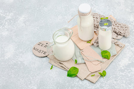 World Milk Day, healthy lifestyle, sustainable morning nutrition. Arrangement of glass milk bottles and jug with eco-friendly props and basil leaves. White trendy background, copy spaceの写真素材