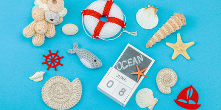 Flat lay composition with crochet marine toys, shells and calendar marking June 8 for World Oceans Day. Nautical handmade decor on a blue background with eco-friendly elements, banner formatの写真素材