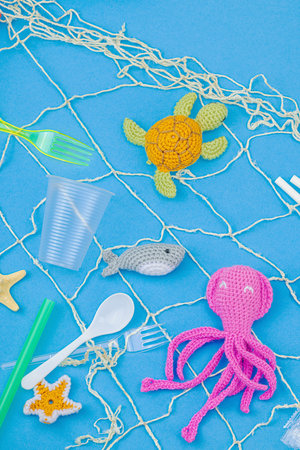 World Oceans Day, water pollution awareness, and environmental education visuals. Handmade crochet marine animals trapped in disposable plastic items and net, blue background, flay lay, top viewの写真素材