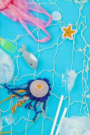 World Oceans Day, water pollution awareness, and environmental education visuals. Handmade crochet marine animals trapped in disposable plastic items and net, blue background, flay lay, top viewの写真素材