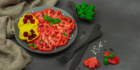 Heirloom sliced Coeur de Boeuf tomato with basil and edible flowers on dark plate. Clean eating, vegan lifestyle and farm-to-table food concept with rustic presentation, banner formatの写真素材