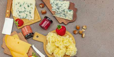 Cheese assortment on rustic background with nuts, strawberries and jam. Includes Tête de Moine, Roquefort, Saint Agur and Gouda on wooden boards, banner formatの写真素材
