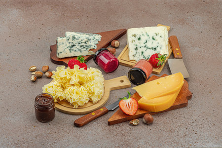 Cheese assortment on rustic background with nuts, strawberries and jam. Includes Roquefort and Gouda on wooden boards, copy spaceの写真素材