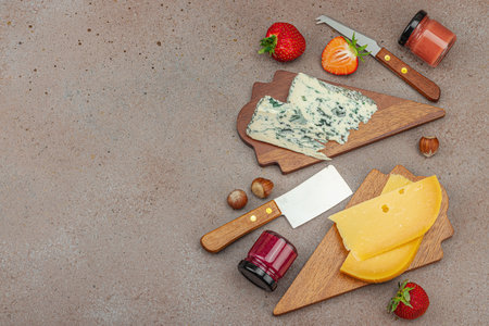 Cheese assortment on rustic background with nuts, strawberries and jam. Includes Roquefort and Gouda on wooden boards, top viewの写真素材