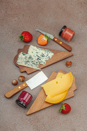 Cheese assortment on rustic background with nuts, strawberries and jam. Includes Tête de Moine, Roquefort, Gouda on wooden boards, top viewの写真素材