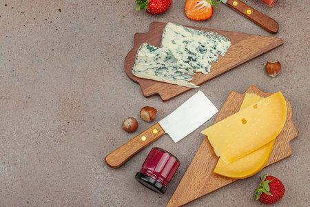 Cheese assortment on rustic background with nuts, strawberries and jam. Includes Roquefort and Gouda on wooden boards, top viewの写真素材