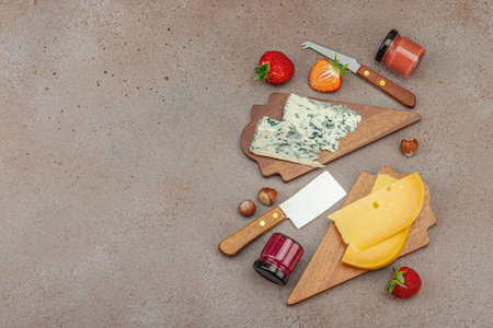 Cheese assortment on rustic background with nuts, strawberries and jam. Includes Roquefort and Gouda on wooden boards, top viewの写真素材