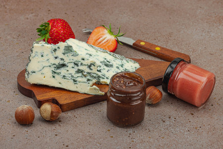 Cheese assortment on rustic background with nuts, strawberries and jam. Includes Roquefort, Saint Agur and Gouda on wooden boards, copy spaceの写真素材