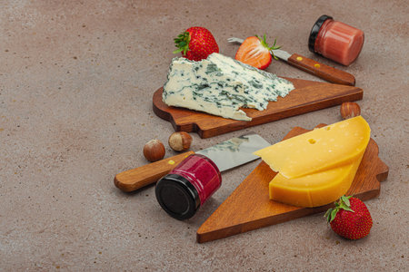 Cheese assortment on rustic background with nuts, strawberries and jam. Includes Roquefort and Gouda on wooden boards, copy spaceの写真素材