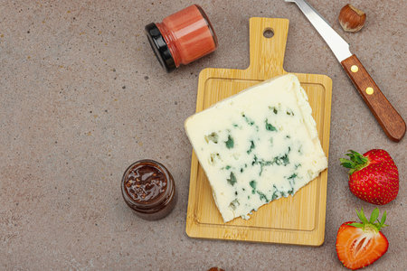 Cheese assortment on rustic background with nuts, strawberries and jam. Includes Roquefort and Gouda on wooden boards, top viewの写真素材