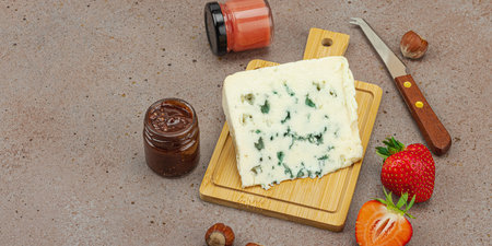 Cheese assortment on rustic background with nuts, strawberries and jam. Includes Gouda on wooden boards, banner formatの写真素材