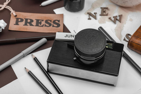 Creative flat lay with vintage camera, press tag, ink bottle, spilled coffee, and messy papers. A...