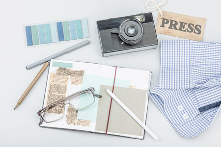 Flat lay of retro journalist essentials on blue background: camera, press badge, notebook, newspaper...