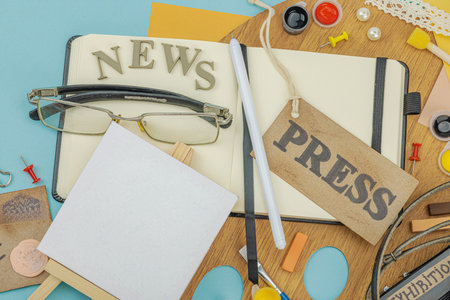 Flat lay of press badge, vintage camera, art supplies, notebook, and exhibition label on a blue background. Concept of artistic journalism and creative investigation, top viewの写真素材