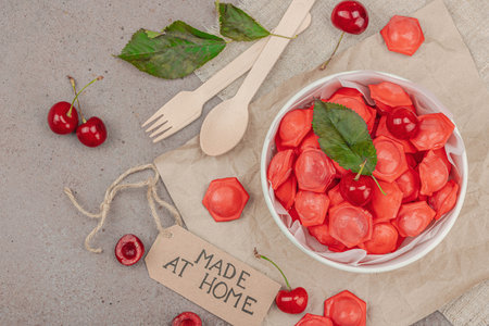 Frozen cherry dumplings in a paper bowl, flat lay composition with fresh cherries, mint, handmade...