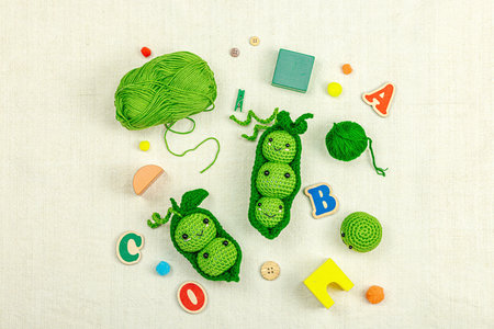Handmade amigurumi peas with colorful baby toys, wooden letters, cotton, and soft textures for early...
