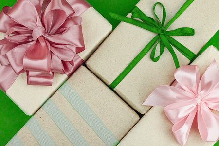 Eco-friendly gift boxes wrapped in kraft paper and decorated with satin ribbons on green background....