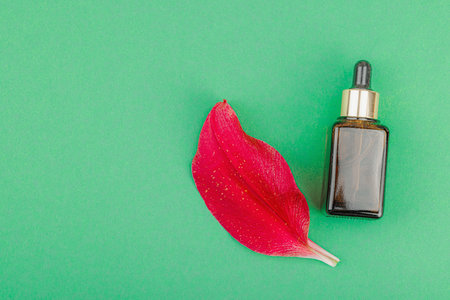 Amber glass dropper bottle with red lily flower petals on green background, minimal natural skincare concept. Beauty routine, flat lay, top viewの写真素材