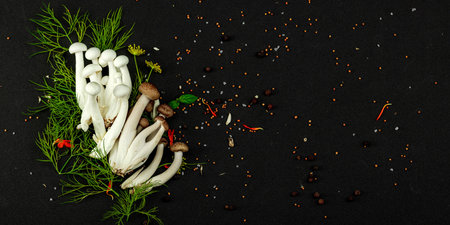Fresh shimeji mushrooms with spices and herbs on black background. Vegan ingredient for healthy...