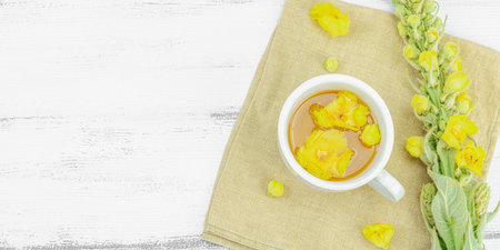 Cup of herbal tea with mullein flowers and leaves on neutral wooden background. Natural light,...