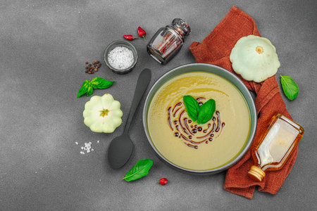 Creamy pattypan squash soup, garnished with basil and balsamic glaze, served in a trendy bowl with fresh ingredients and spices. Dark stone concrete background, top viewの写真素材