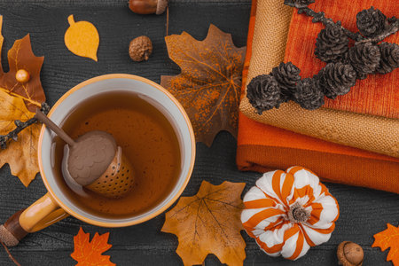 Cozy autumn still life with a cup of tea, handmade fabric pumpkins, acorns, pine cones, fall leaves,...