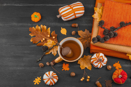 Cozy autumn still life with a cup of tea, handmade fabric pumpkins, acorns, pine cones, fall leaves,...