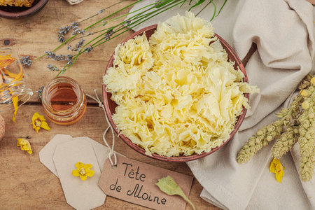 Rustic still life with Tete de Moine cheese, honey, and dried herbs on a wooden table. Warm light and vintage atmosphere in apothecary style, flat lay, top viewの写真素材