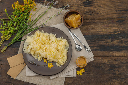 Rustic still life with cheese, honey, and dried herbs on a wooden table. Warm light and vintage...