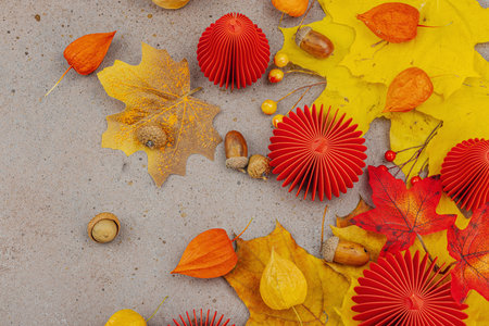 Autumn still life with red paper pumpkins, acorns, yellow maple leaves, and physalis on a textured...