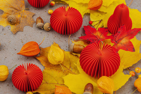 Autumn still life with red paper pumpkins, acorns, yellow maple leaves, and physalis on a textured background. Cozy seasonal composition, slow living style, close upの写真素材