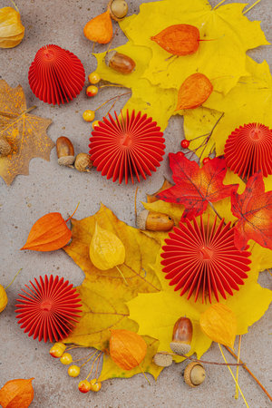Autumn still life with red paper pumpkins, acorns, yellow maple leaves, and physalis on a textured background. Cozy seasonal composition, slow living style, top viewの写真素材