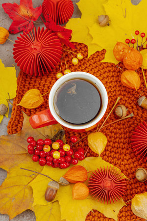 Autumn still life with a red cup of tea, viburnum berries, acorns, yellow maple leaves, and crafted decor in warm cozy tones, symbolizing slow living and handmade comfort, top viewの写真素材