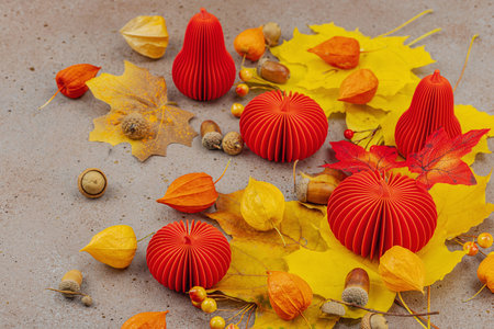 Autumn still life with red paper pumpkins, acorns, yellow maple leaves, and physalis on a textured background. Cozy seasonal composition, slow living style, close upの写真素材