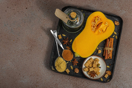 Half butternut squash on a dark tray with baking ingredients. Brown sugar, cinnamon sticks, ginger, nutmeg. Essential spices for traditional autumn pie and dessert recipes, warm brown background, top viewの写真素材
