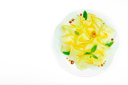Thinly sliced melon carpaccio appetizer with fresh mint and balsamic sauce drops on a white plate. Gourmet isolated food design for healthy dining, top viewの写真素材