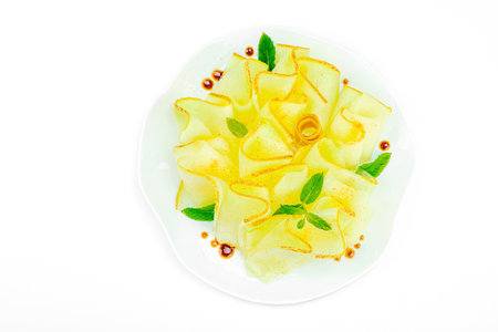 Thinly sliced melon carpaccio appetizer with fresh mint and balsamic sauce drops on a white plate. Gourmet isolated food design for healthy dining, top viewの写真素材