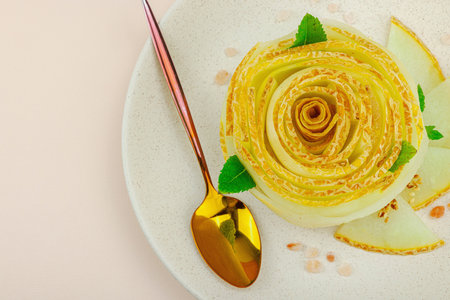Elegant melon carpaccio dessert shaped like a flower, garnished with mint, spices and pink salt crystals on a ceramic plate. Light peach background, top viewの写真素材