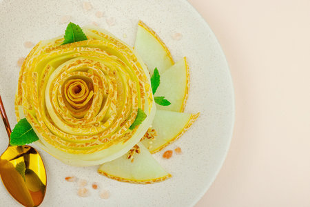 Elegant melon carpaccio dessert shaped like a flower, garnished with mint, spices and pink salt crystals on a ceramic plate. Light peach background, top viewの写真素材