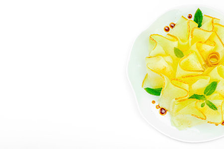 Thinly sliced melon carpaccio appetizer with fresh mint and balsamic sauce drops on a white plate. Gourmet isolated food design for healthy dining, top viewの写真素材