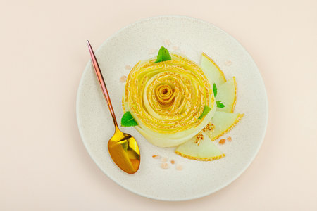 Elegant melon carpaccio dessert shaped like a flower, garnished with mint, spices and pink salt crystals on a ceramic plate. Light peach background, top viewの写真素材