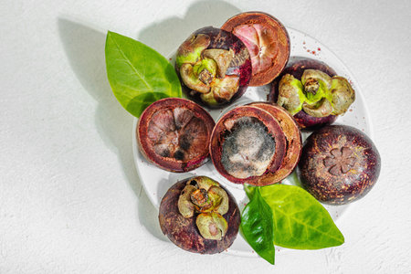 Mangosteen fruits on a white plate with some pieces affected by gray-black mold, highlighting critical issues of food spoilage, quality control, and improper storageの写真素材