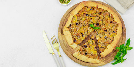 Baked rustic zucchini galette slices on garnished with fresh basil. Homemade savory vegetable tart served on a textured light background for a gourmet meal, banner formatの写真素材