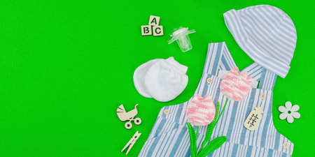 Hypoallergenic newborn set. Baby clothing, striped romper and hat. Handmade crochet tulips and wooden nursery decor on a green background, eco-friendly lifestyle, flat lay, banner formatの写真素材