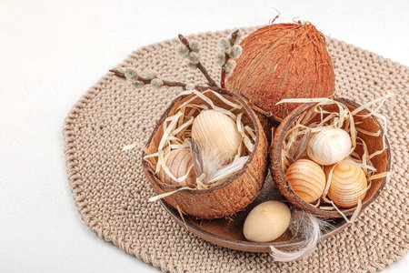 Easter decoration with wooden eggs in coconut shells, pussy willow branches and feathers on knitted...