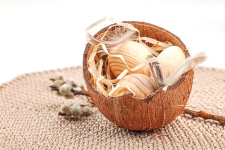 Easter decoration with wooden eggs in coconut shells, pussy willow branches and feathers on knitted...