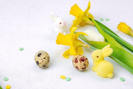 Easter background with yellow daffodils, white tulips, quail eggs, and cute decorative bunnies on a light textured surface. Spring floral arrangement for a holiday greeting card, copy spaceの写真素材