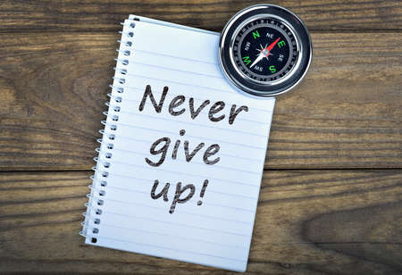 Never give up text and metallic compass on wooden tableの写真素材